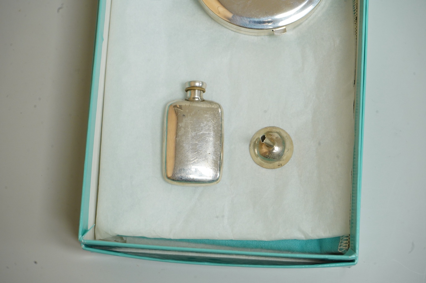A small modern Tiffany & Co sterling scent flask, 44mm, together with a Tiffany & Co sterling compact, diameter 64mm and a small unmarked white metal funnel, with an associated Tiffany & Co box.